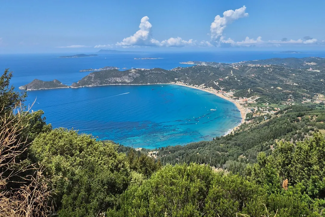 Weite Bucht von oben: türkisfarbenes Wasser, bewaldete Hügel, Inseln am Horizont